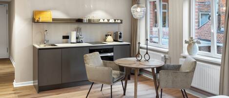 Cocina moderna con una isla central, una zona de comedor con dos sillas y un ventanal con vista a un edificio de ladrillo.