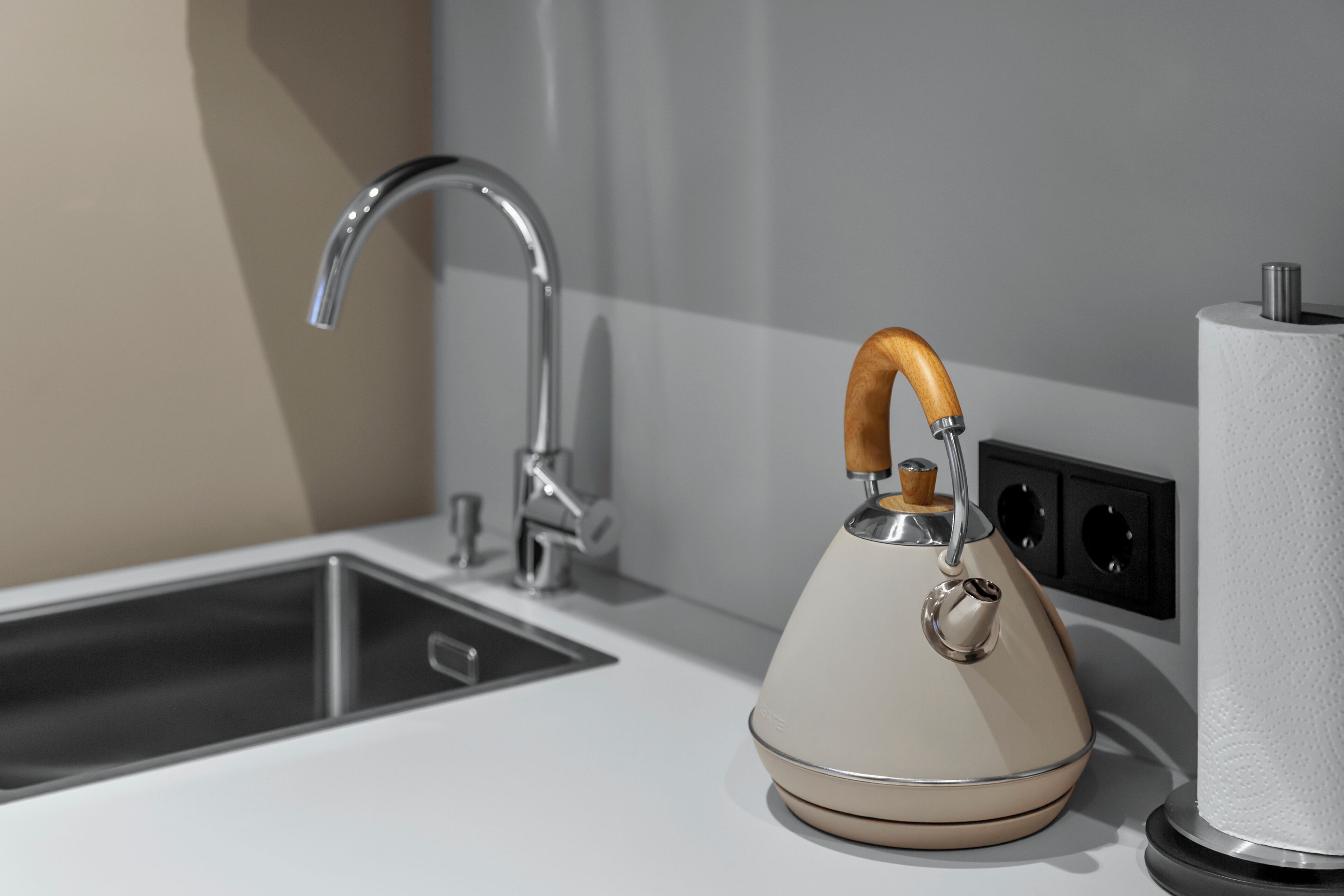 Una cocina con un grifo moderno, un hervidor y un dispensador de toallas de papel.