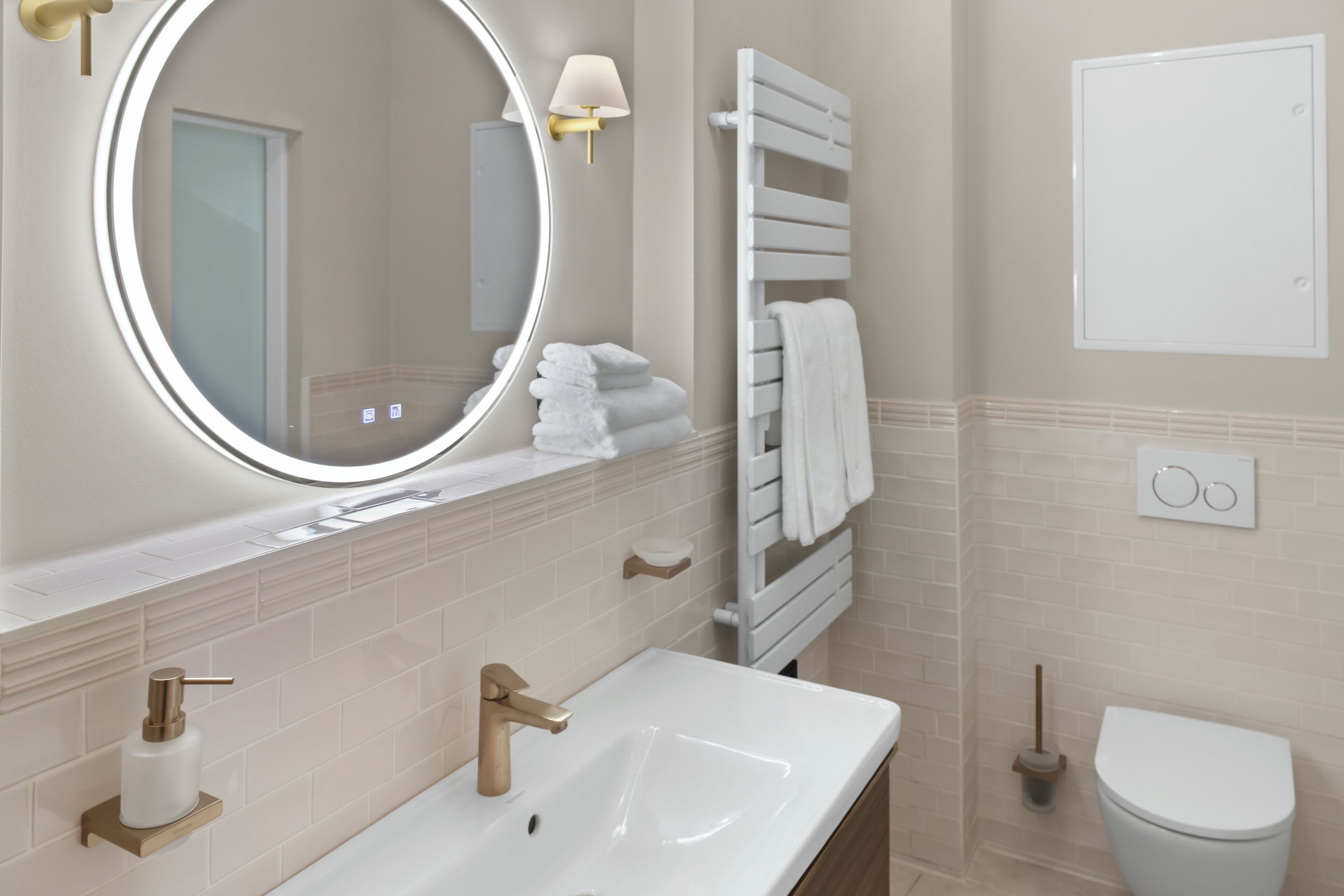 Une salle de bain avec un lavabo blanc, un miroir rond, un porte-serviettes et des toilettes.
