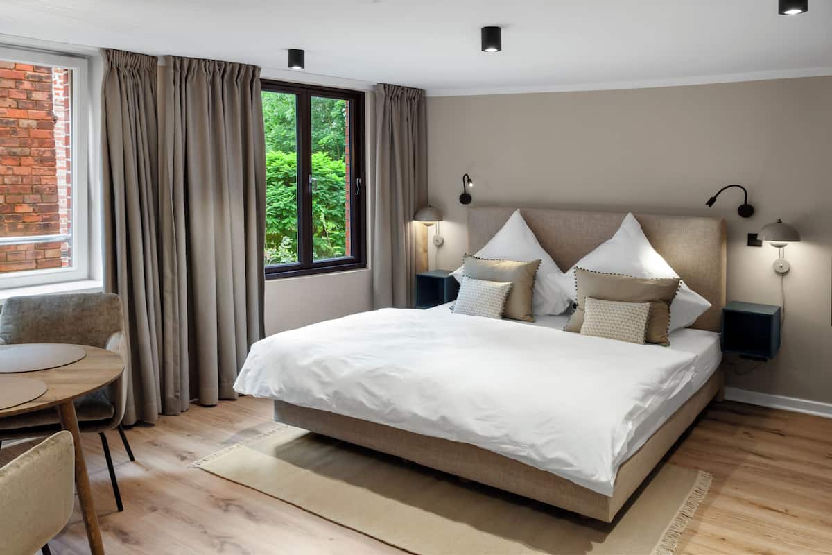 A modern bedroom with a large bed, a round table, and a view of greenery through a window.