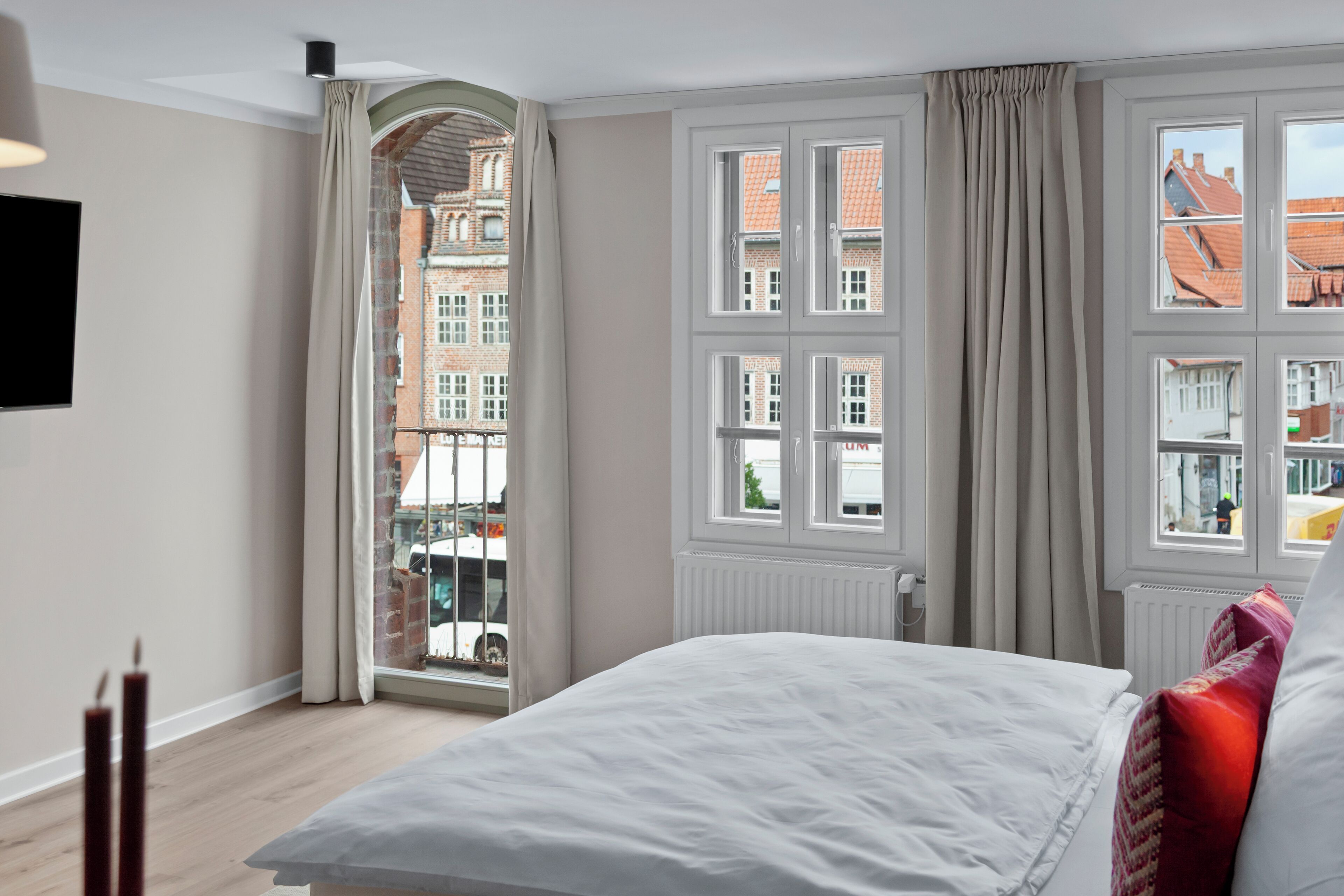 Ein Hotelzimmer mit einem großen Bett, Blick auf eine Stadt durch ein Fenster und einem Heizkörper an der Wand.