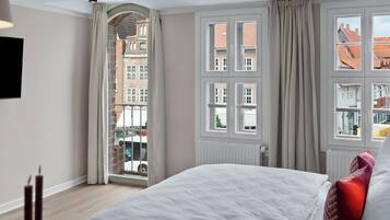 Ein Hotelzimmer mit einem großen Bett, Blick auf eine Stadt durch ein Fenster und einem Heizkörper an der Wand.