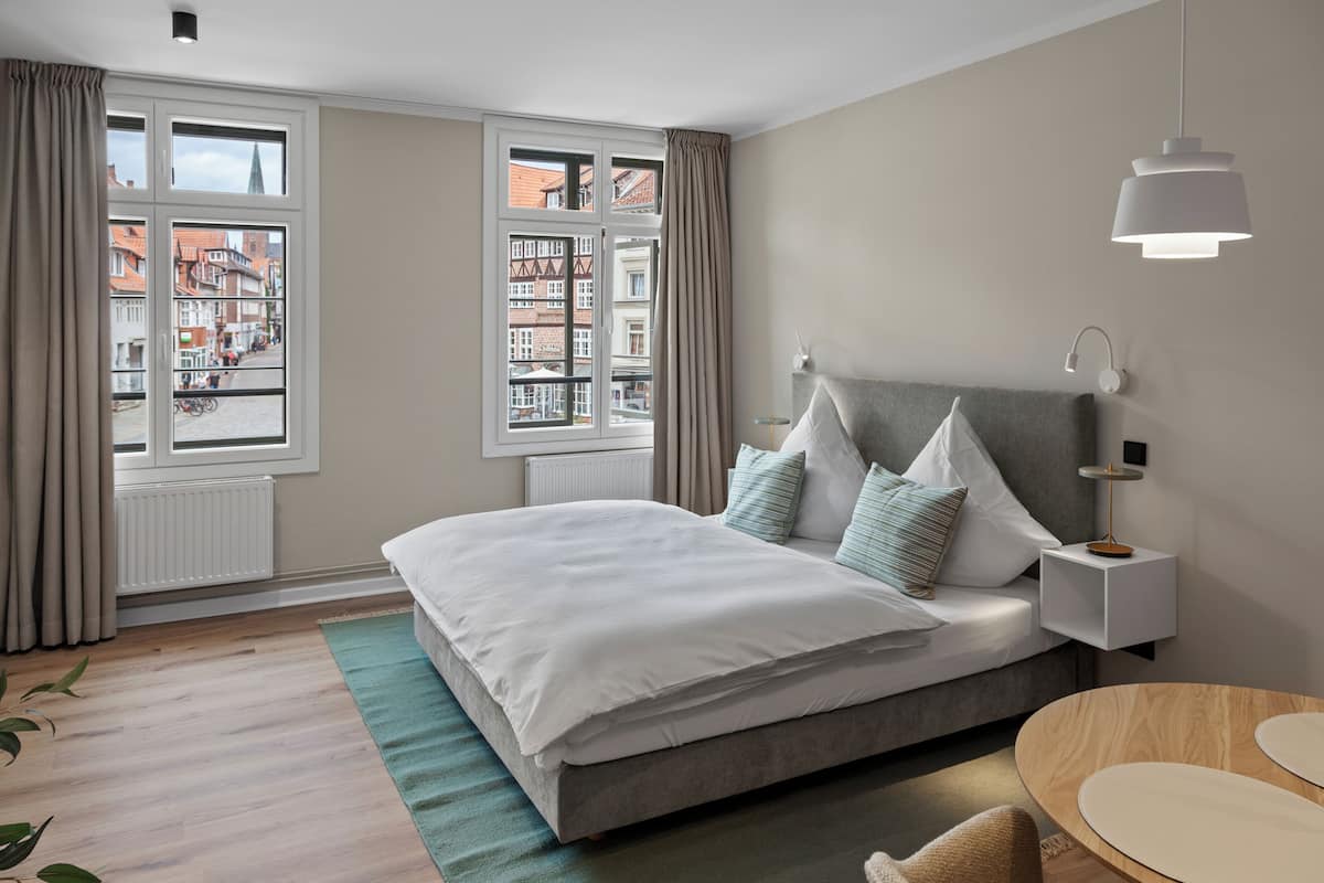 A modern bedroom with a large bed, a bedside table, a nightstand, and a view of the city through large windows.