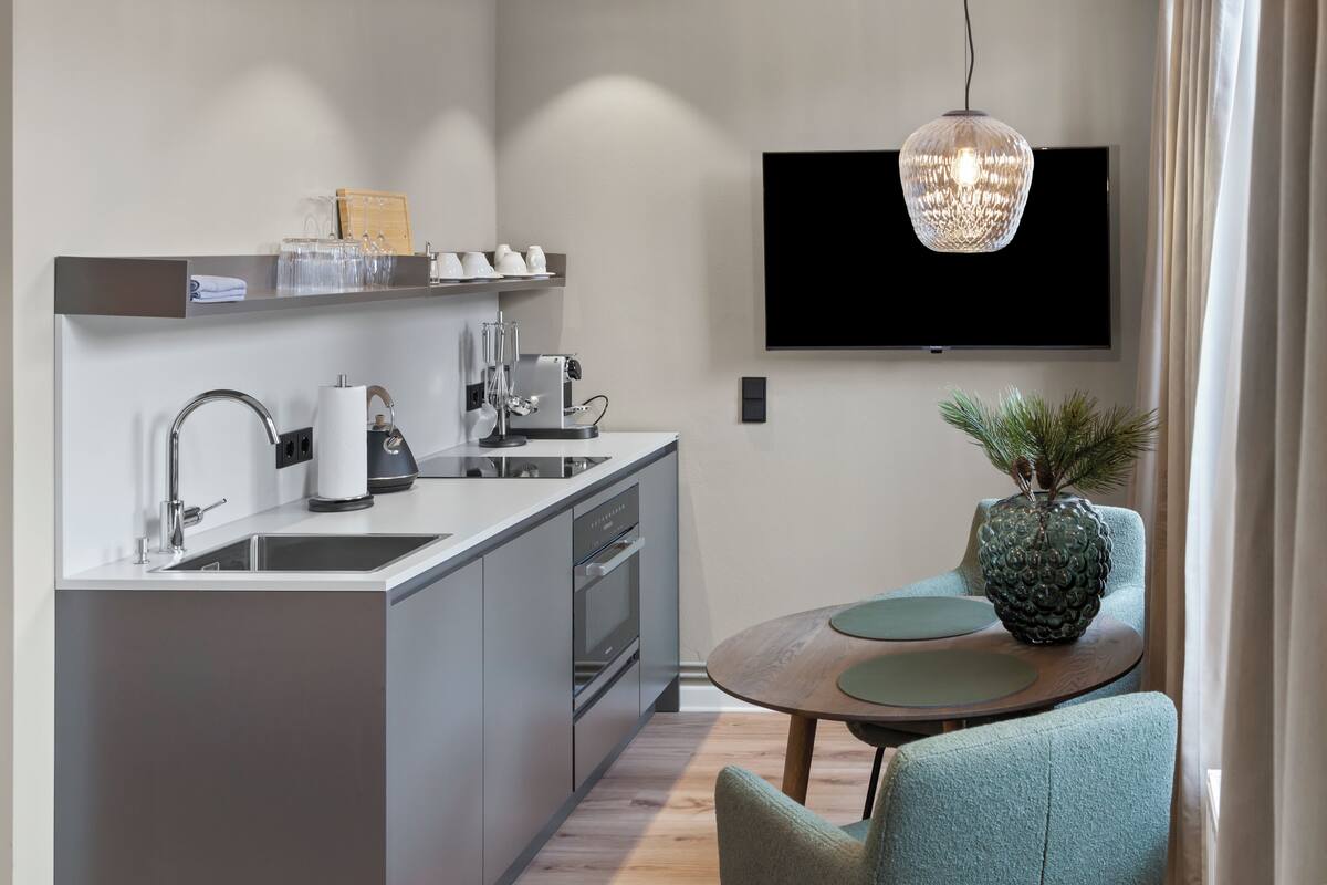 A modern kitchen with a built-in oven, a sink, and a coffee maker. There is a flat-screen TV mounted on the wall above the kitchen counter.