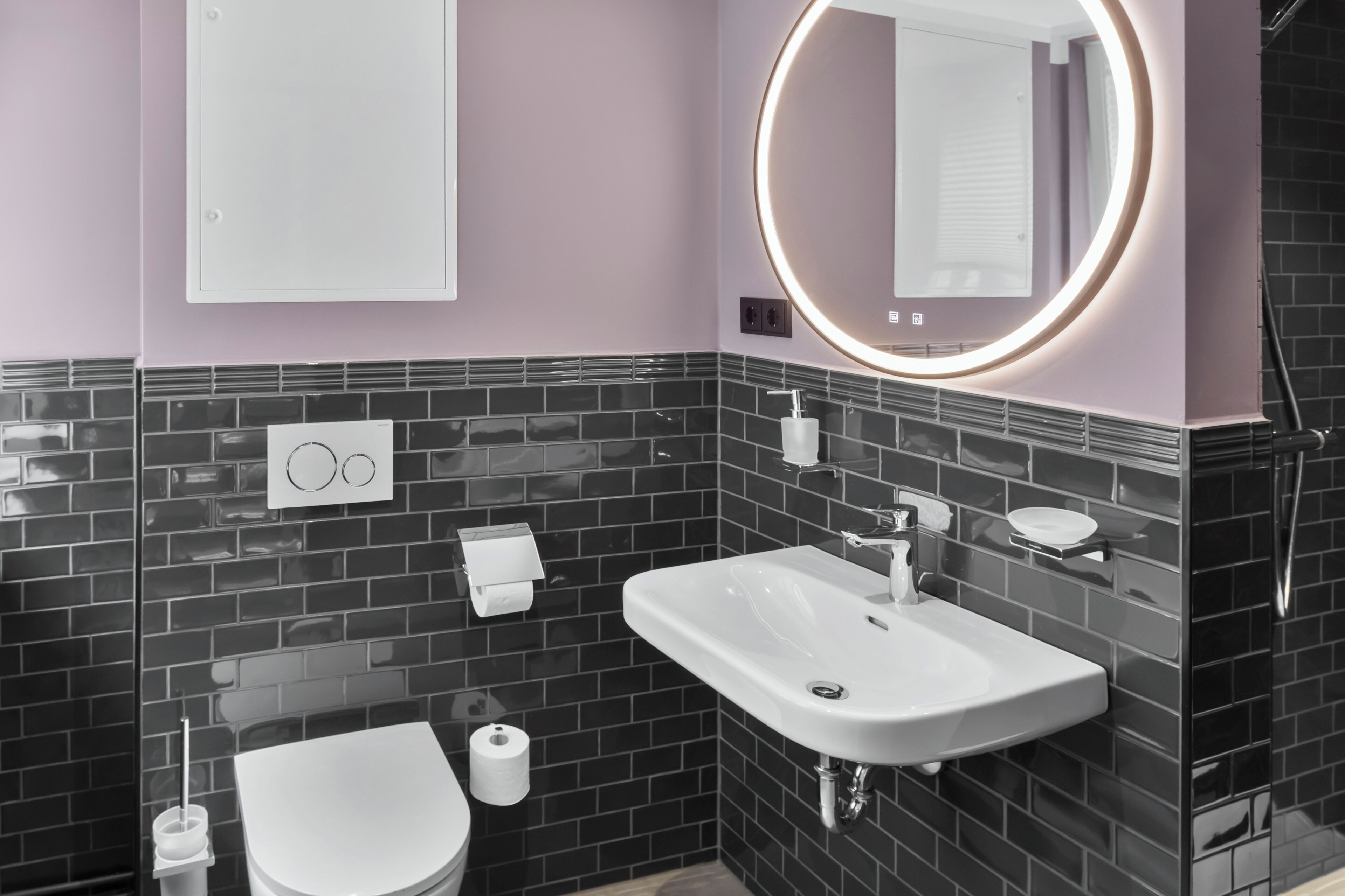 Un baño moderno con un lavamanos blanco, un inodoro y un espejo con luz circular.
