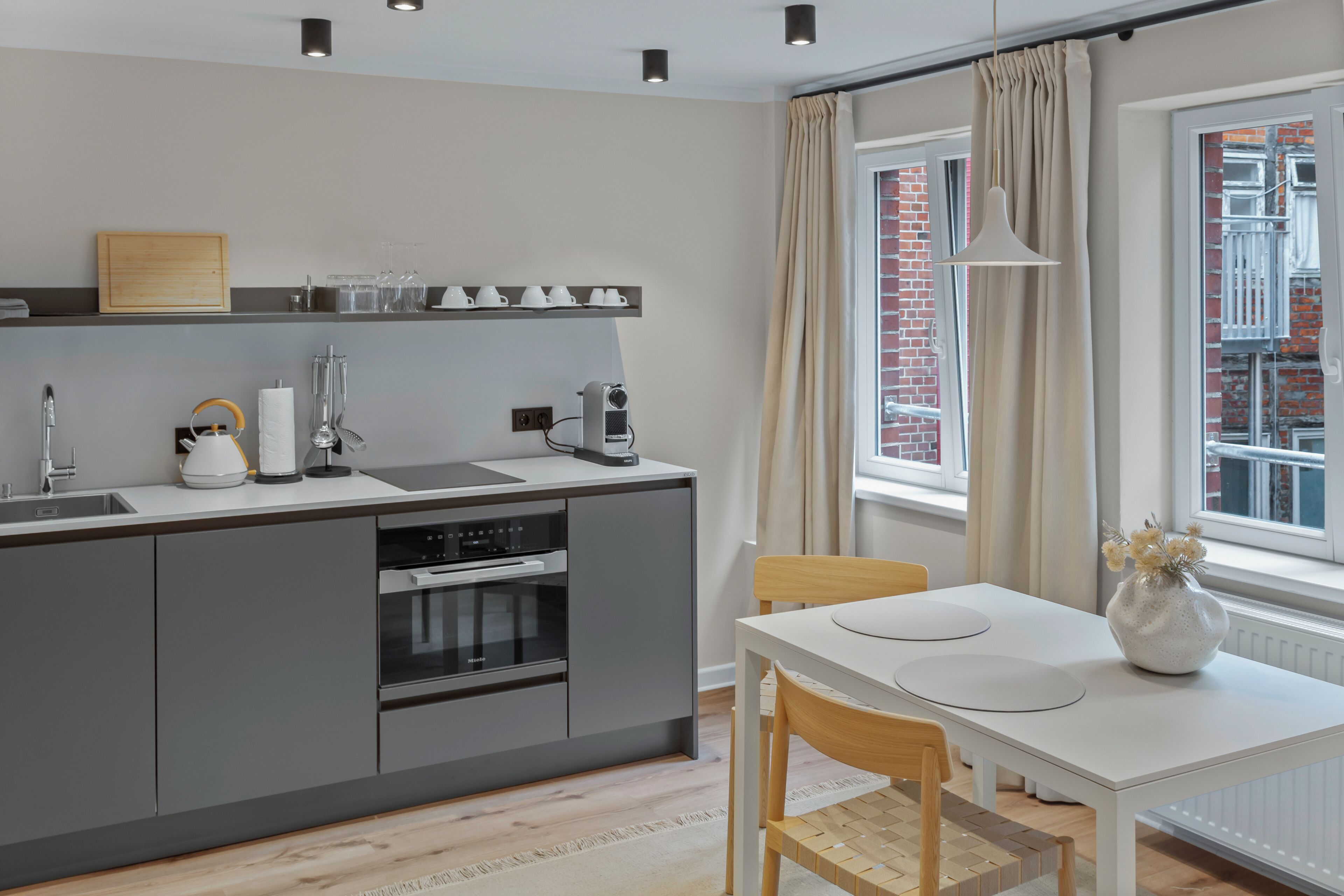 Una cocina moderna con armarios grises, una encimera blanca y una zona de comedor con mesa y sillas blancas.