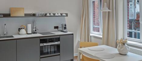 Una cocina moderna con armarios grises, una encimera blanca y una zona de comedor con mesa y sillas blancas.