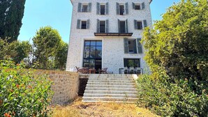 Un bâtiment à deux étages, doté d’une façade en pierre, de nombreuses fenêtres avec volets et d’un escalier menant à l’entrée.