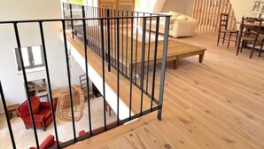 Un vaste espace de vie doté d’un plancher en bois, d’un canapé, d’une table à manger avec des chaises et d’un escalier muni d’une rampe.