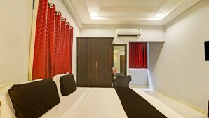 A hotel room with a large bed, red curtains, a wardrobe, and an air conditioning unit.