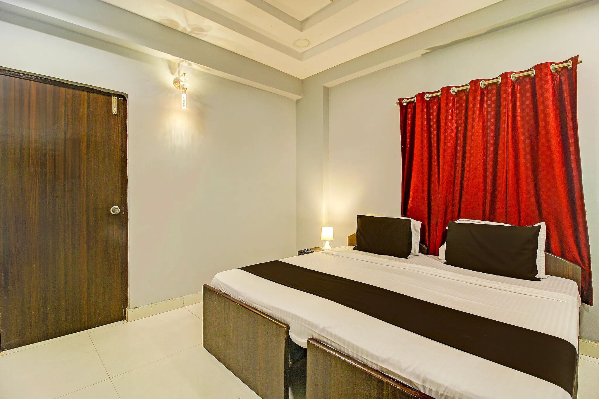 A hotel room with a large bed, a wooden door, and a red curtain.