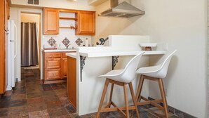 A kitchen with wooden cabinets, a white countertop, two white bar stools, and a patterned rug.