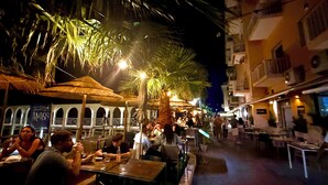 An outdoor dining area with tables and chairs, palm trees, and thatched umbrellas. - Experience Authentic Italian Elegance Between Rome and the Sea (Civitavecchia)