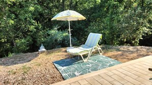 Een patio met een houten terras, een kamerkleed met patroon, een gestreepte loungestoel en een decoratieve parasol.