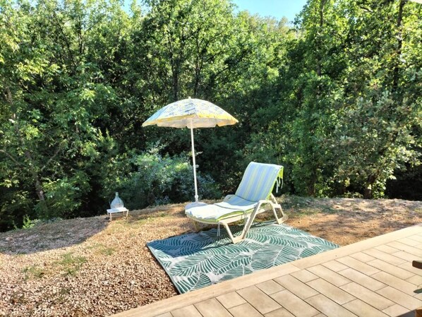 Ein Patio mit Holzdeck, einem gemusterten Teppich, einem gestreiften Liegestuhl und einem Zierparaschirm.