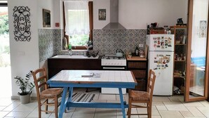 Een keuken met een blauwe tafel, twee houten stoelen, een fornuis, een koelkast en een raam met gordijn.