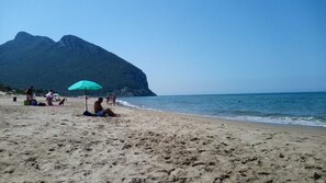 Ein Strand mit Menschen, einem grünen Sonnenschirm und einem Berg im Hintergrund.