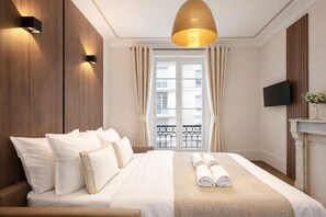 Ett hotellrum med en stor säng, en platt-TV, en öppen spis och en balkong med gardiner.