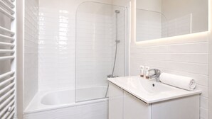 A modern bathroom with a bathtub, shower, and a vanity with a mirror. - 1609 CroixNivert (Paris)