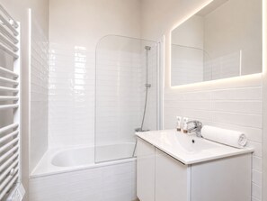 A modern bathroom with a bathtub, shower, and a vanity with a mirror. - 1609 CroixNivert (Paris)