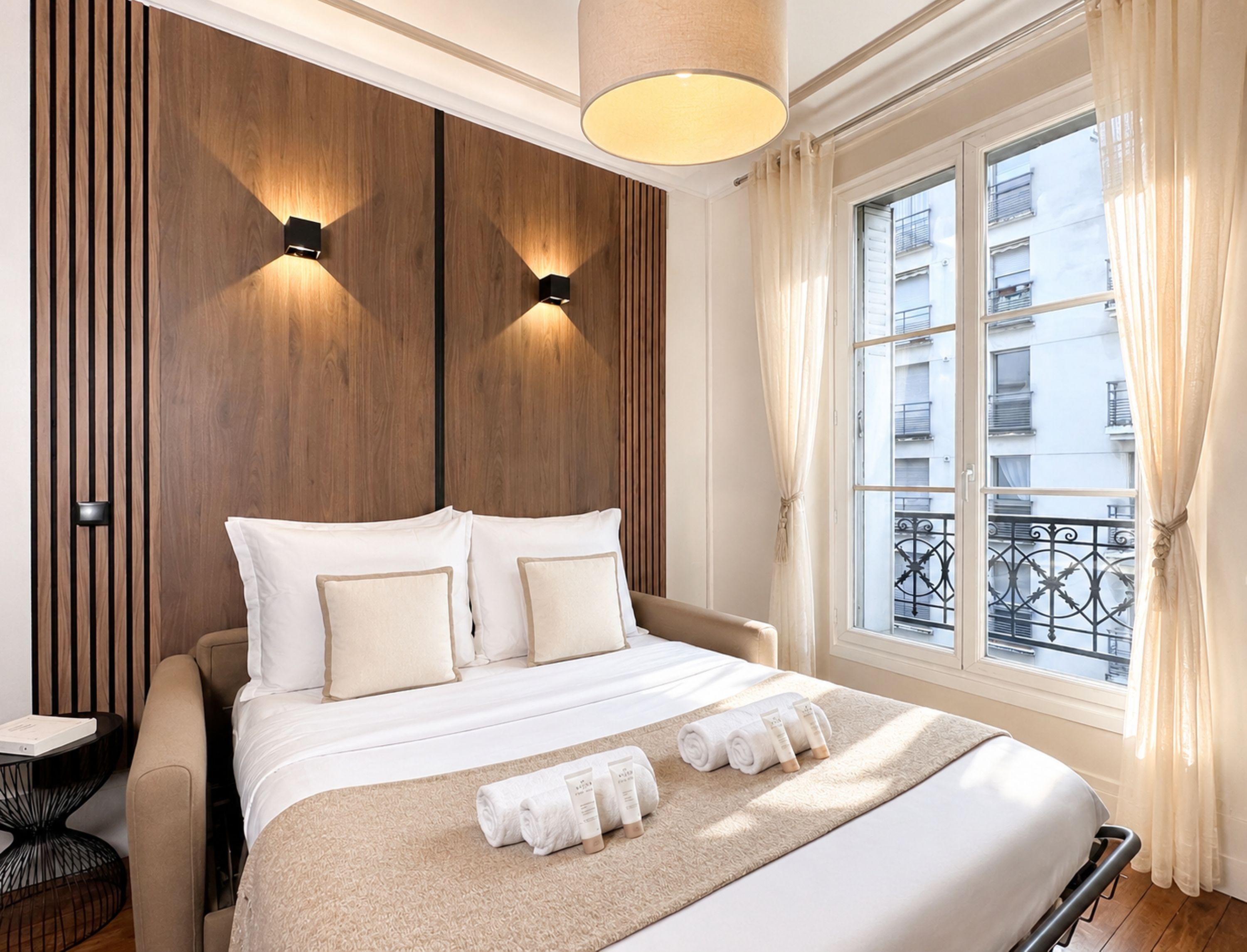 A hotel room with a bed, a bedside table, a lamp, and a window with curtains.
