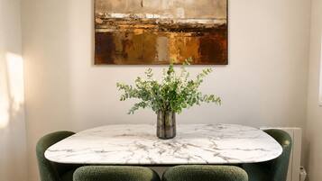 A dining area with a marble table, green upholstered chairs, and a vase with white flowers.