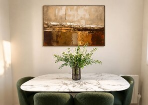Een eetgedeelte met een marmeren tafel, groene bekleden stoelen en een vaas met witte bloemen.