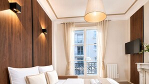 A hotel room with a bed, a television, a fireplace, and a view of the outside. - 1609 CroixNivert (Paris)
