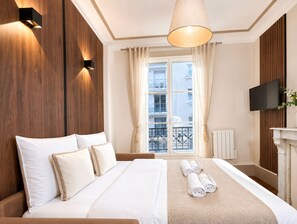 A hotel room with a bed, a television, a fireplace, and a view of the outside. - 1609 CroixNivert (Paris)