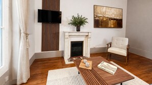 Een moderne woonkamer met een open haard, een televisie, een schilderij en een comfortabele fauteuil.