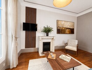 Een moderne woonkamer met een open haard, een televisie, een schilderij en een comfortabele fauteuil.