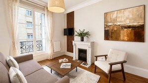 Een woonkamer met een bank, fauteuil, open haard, televisie en kunstwerken.