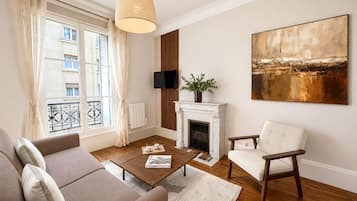A living room with a sofa, armchair, fireplace, TV, and artwork.