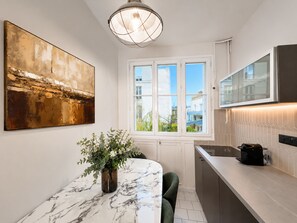 Een moderne keuken met een marmeren aanrecht, een potplant, een groot abstract schilderij en een raam met uitzicht op gebouwen.