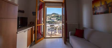 Un espacio habitable compacto con kitchenette, sofá y vistas a un pueblo en la ladera a través de un ventanal grande.