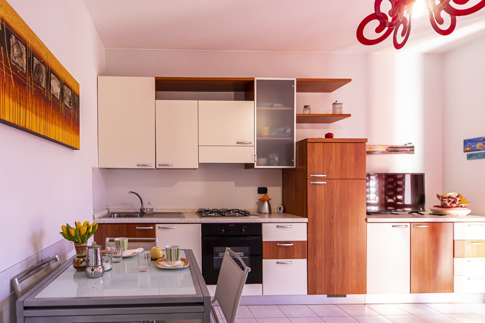 A modern kitchen with white cabinets, a glass dining table, and a red decorative light fixture.