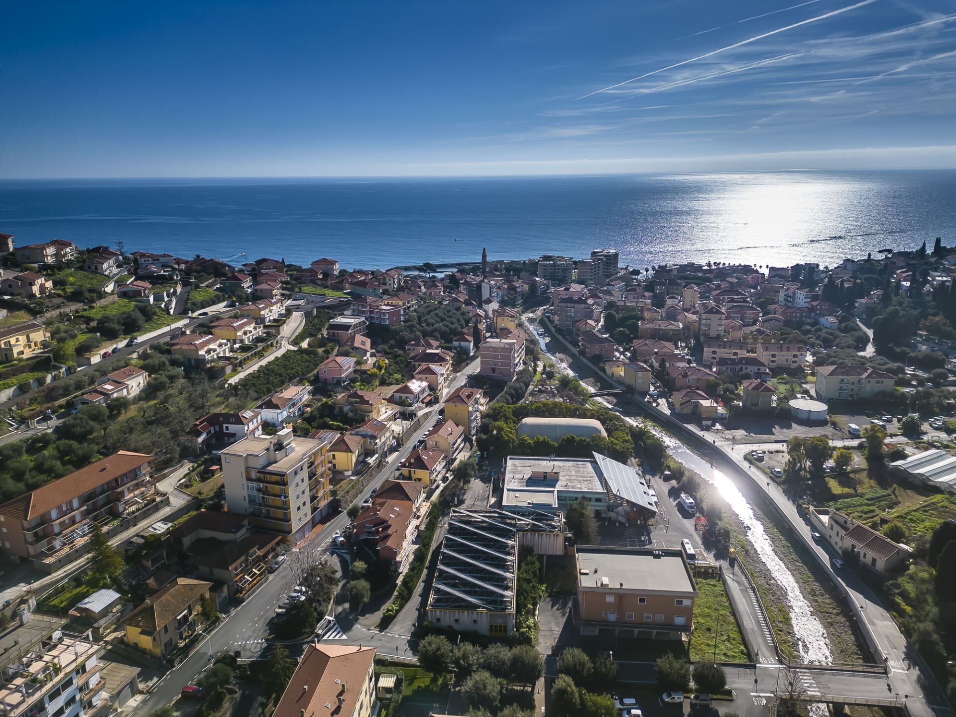 Vista aérea de un pueblo costero con edificios residenciales, una carretera principal y una vía ferroviaria.