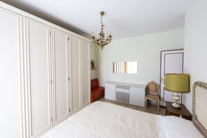 Una camera da letto con un letto, una scrivania, una sedia, un armadio, un lampadario e una lampada.