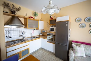 Une cuisine compacte équipée d’une cuisinière à gaz, d’un four à micro-ondes et d’un réfrigérateur, un coin repas avec une table et des chaises, et un salon avec un canapé.