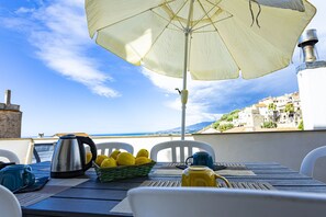 A table with a kettle, a basket of lemons, and a blue mug, under a large umbrella, overlooking a coastal town. - Three-room apartment with sea view terrace (Cipressa)