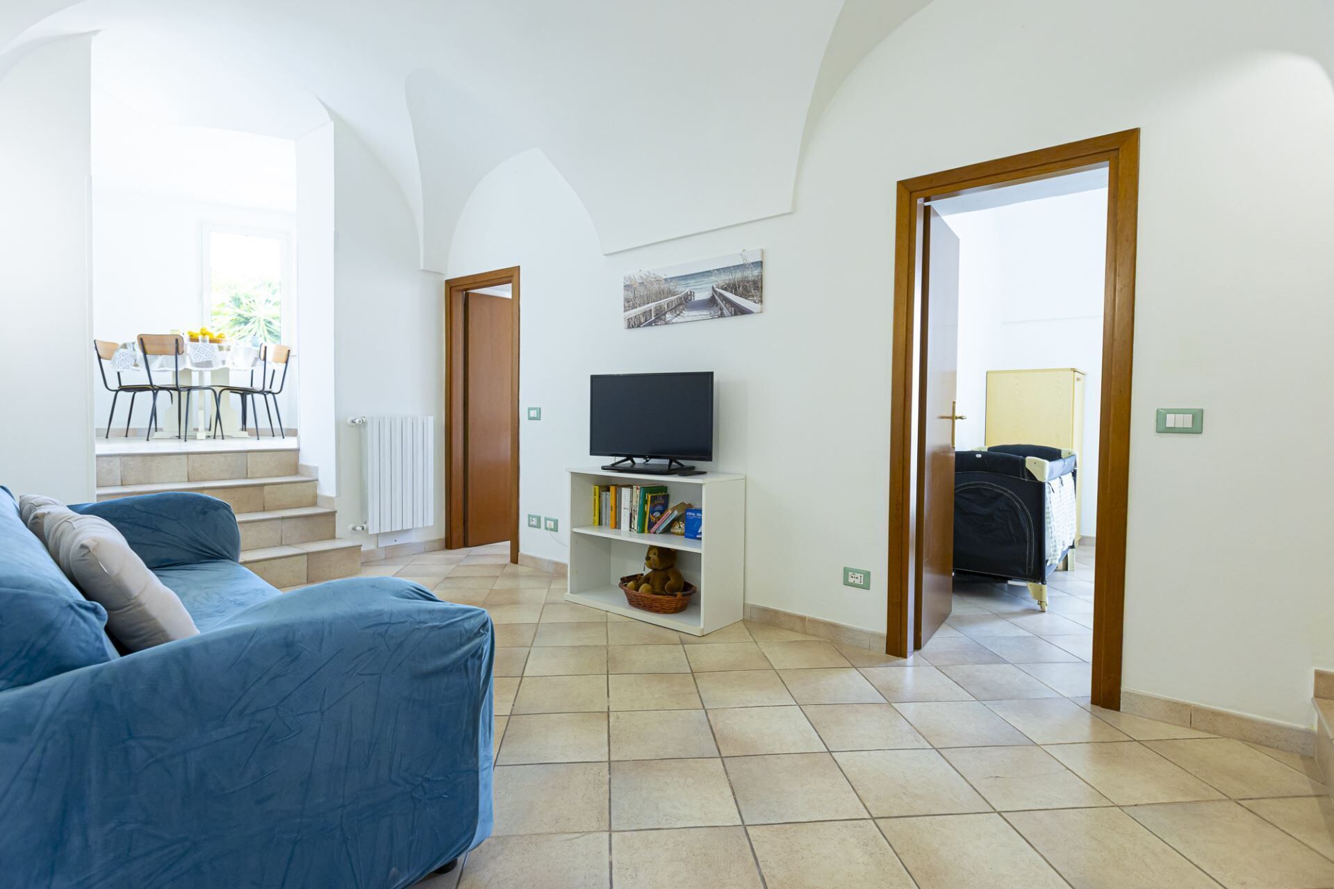 Una sala de estar con un sofá, un televisor sobre un mueble, una estantería y una escalera que sube a un piso superior.