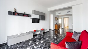 A modern living room with a black and white marble floor, a grey sofa with red cushions, a white console table, and a TV mounted on the wall.