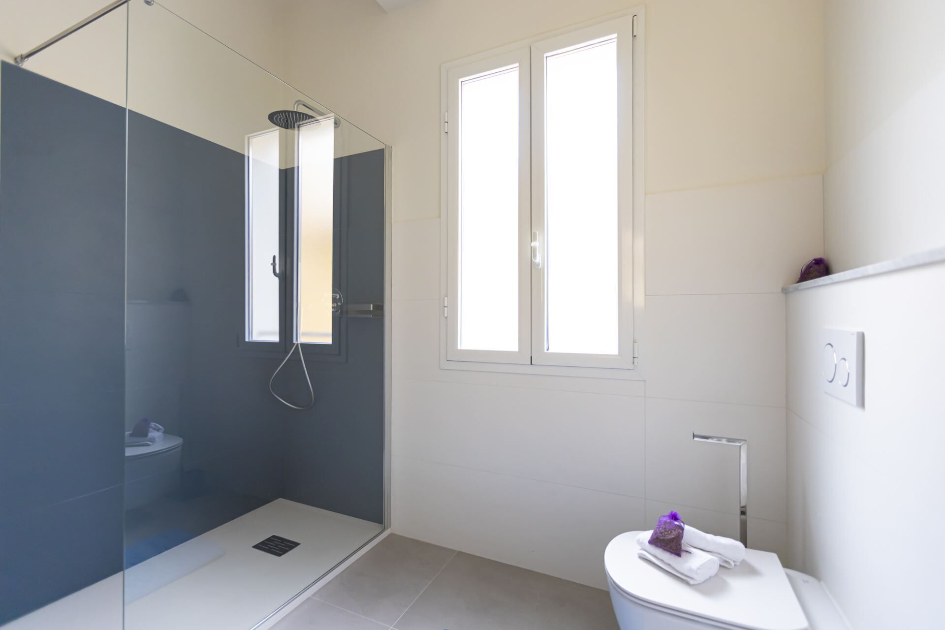 A modern bathroom with a glass-enclosed shower, a toilet, and a window providing natural light.