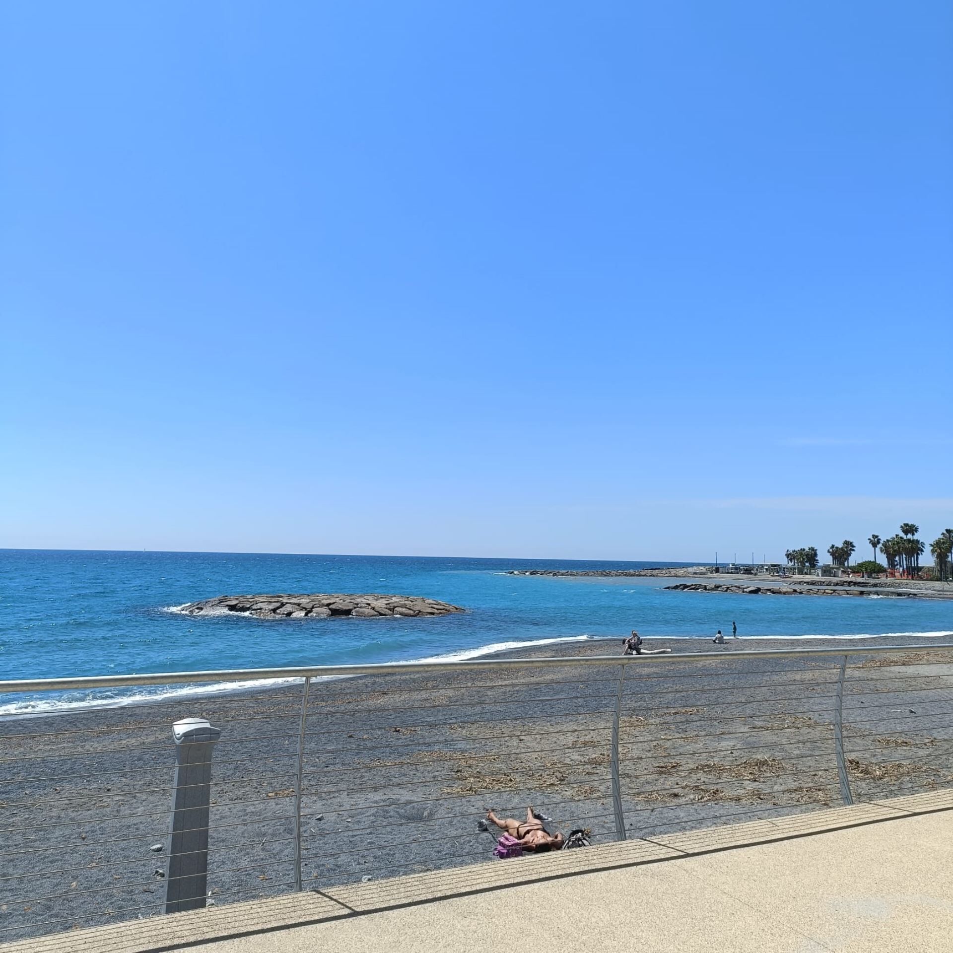 Une plage avec un promontoire rocheux, une zone délimitée par une clôture et un ciel bleu dégagé.