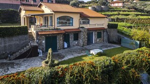 A two-story house with a tiled roof, stone walls, and a small garden area with outdoor seating.