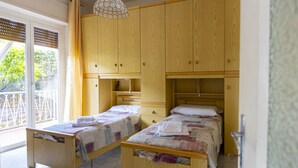 A room with two wooden beds, a large wooden wardrobe, and a balcony with a view of greenery.