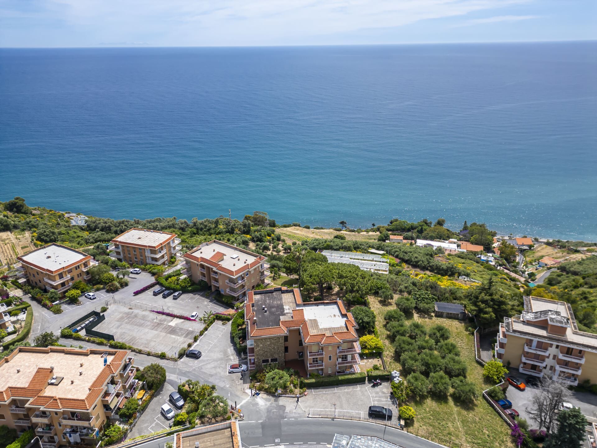 A coastal residential area with apartment buildings, a parking lot, and a view of the sea.