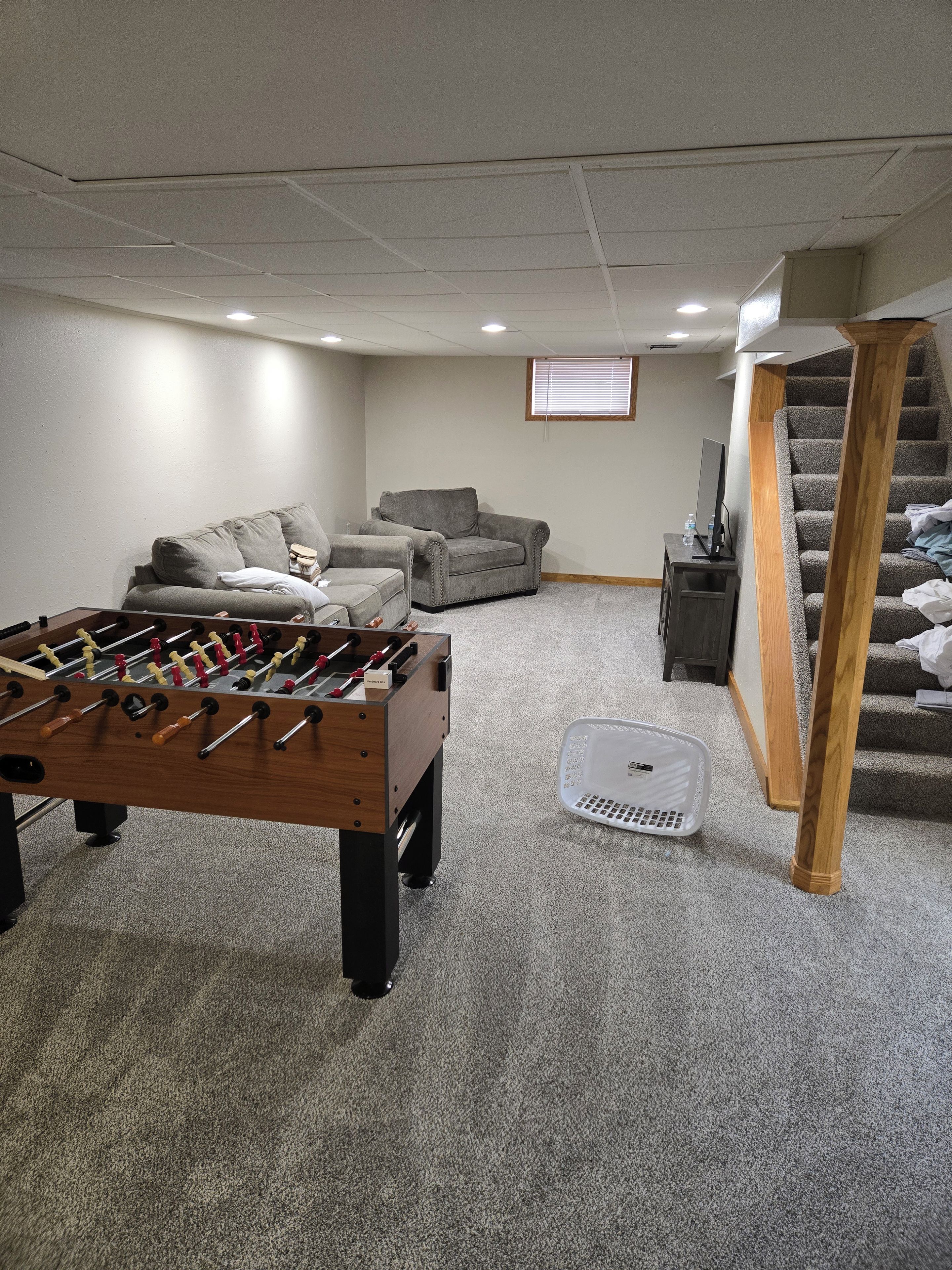 Une pièce avec une table de baby-foot, un canapé, un escalier et une fenêtre.