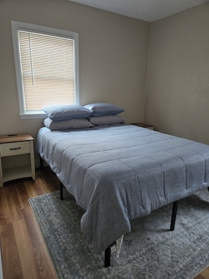 A bedroom with a bed, nightstand, and window with blinds. - Fully updated 3-bedroom home near college and hospitals. (Sioux City)