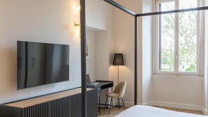 A bedroom with a bed, a desk with a chair, a TV, and a window with a view of trees. - Rental in Rome Mellini View Apartment (Rome)